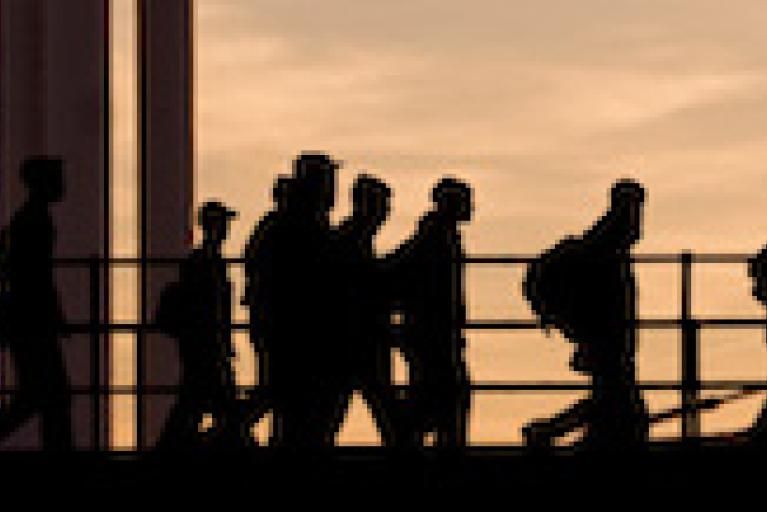 A landscape image of workers safety works walking in silhouette against a sepia toned background. 