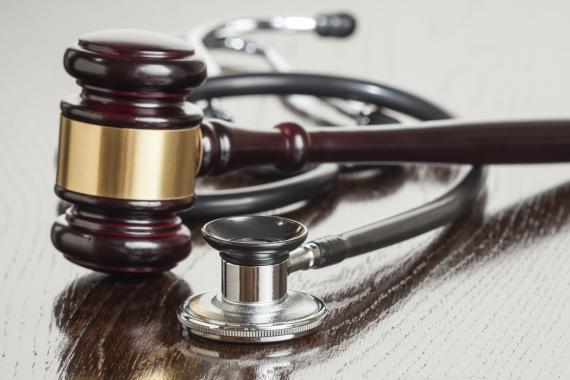 A stock image of a judge's gavel and a stethoscope lying on a wooden desk.